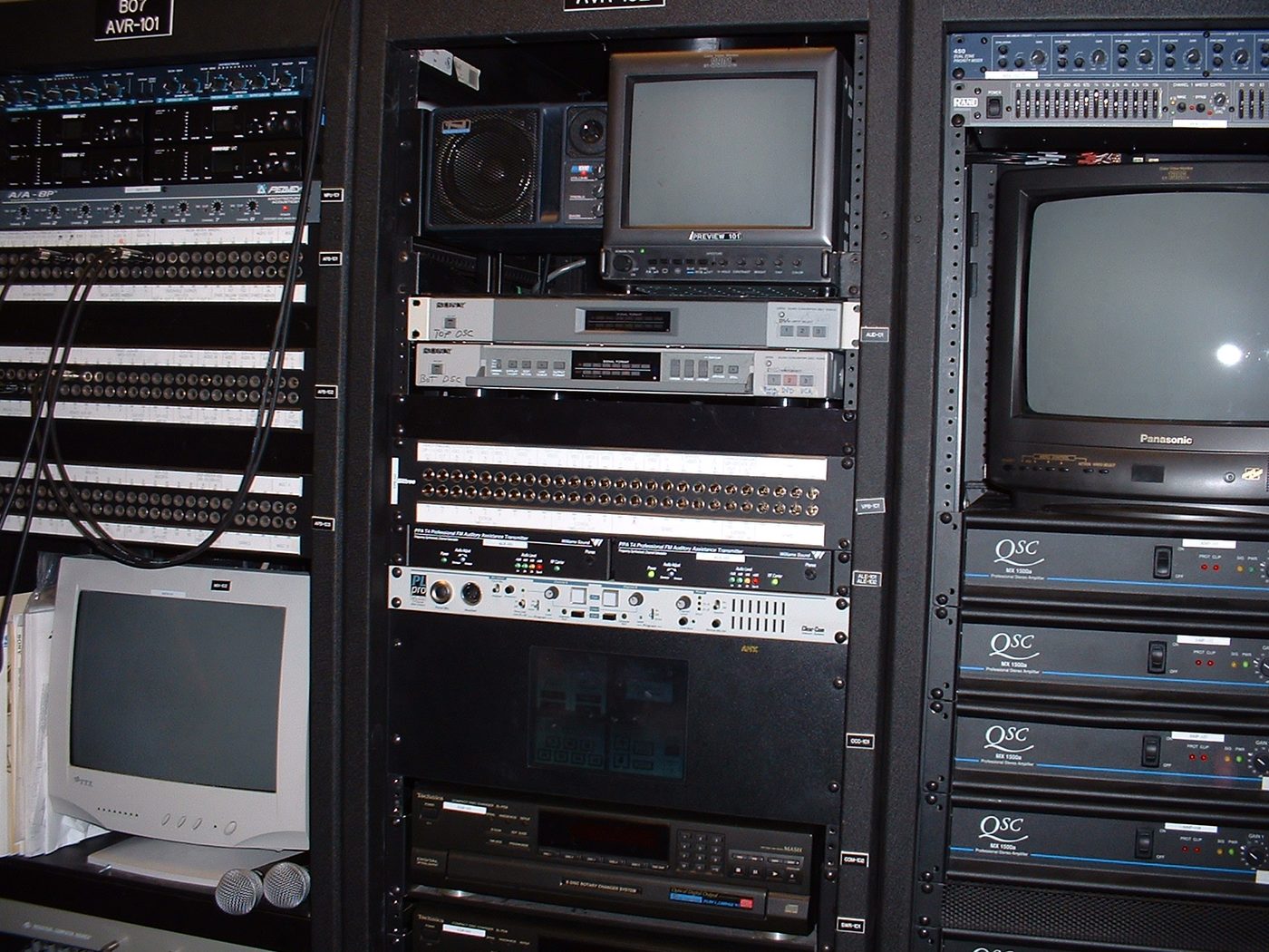 Globe Theatre audiovisual equipment racks with patch bays, monitors, processors, and QSC amplifiers
